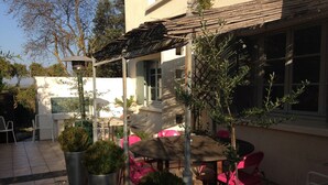 Une terrasse extérieure avec une table et des chaises, entourée de plantes en pot et agrémentée d’une pergola.