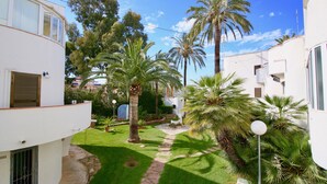 A residential area with white buildings, a paved pathway, and palm trees. - Apartment in beachfront Albaranas (Denia)