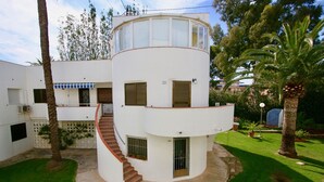 A two-story building with a curved staircase, a balcony, and a small garden area with palm trees. - Apartment in beachfront Albaranas (Denia)