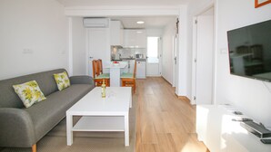 A modern living room with a grey sofa, a white coffee table, and a TV on a stand. - Apartment in beachfront Albaranas (Denia)