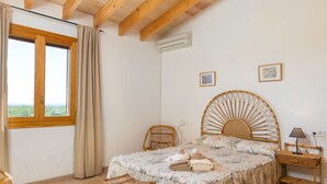 A bedroom with a large bed, a chair, a bedside table, and a window with curtains. - Can Toni - Mallorcan style country house in Binissalem (Lloseta)