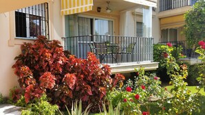 A balcony with outdoor furniture, a yellow-striped awning, and a variety of plants including red-leafed shrubs and roses. - Apartment in Torremolinos (La Carihuela area) Erisa 1. (Torremolinos)