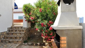 Un estrecho sendero de piedra que conduce a un edificio blanco con una zona de barbacoa de ladrillo y una pequeña escalera.