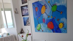 Un comedor con una mesa de vidrio, sillas blancas y un cuadro colorido en la pared.