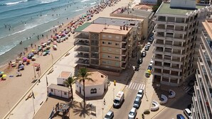 Un paisaje urbano costero con una playa extensa bordeada de sombrillas de colores y edificios.