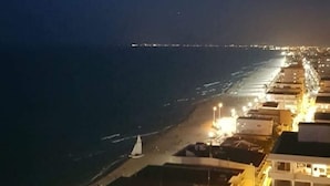 Un hotel frente al mar con varios pisos, vistas a la playa y el perfil distante de una ciudad.