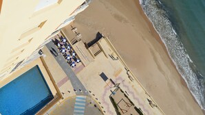 Vista aérea de un hotel frente a la playa, con piscina, sillas de playa y sombrillas.