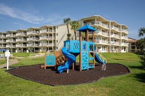 A playground with a blue slide and climbing area, surrounded by a landscaped area with palm trees. - CRC 1303 - Silver Oceanfront Extended Balcony (St Augustine)
