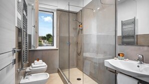 Ein modernes Badezimmer mit einer Duschkabine, einem Waschbecken und einem Fenster mit Ausblick nach draußen.
