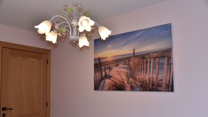 Een kamer met een houten deur, een aan de muur hangend schilderij van een strandtafereel en een decoratieve lamp.