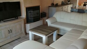 Een woonkamer met een witte bank, een televisie, een open haard en een bijzettafeltje.