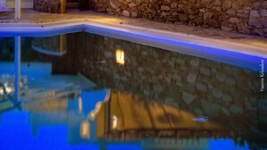 Eine Steinmauer vor einem Gebäude mit weißen Wänden und einem geneigten Dach, vor dem sich ein Pool befindet.