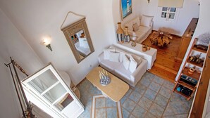 Ein geräumiger Wohnbereich mit einer Couch, einem Couchtisch und einem Spiegel. An der Wand hängt ein Gemälde und der Boden ist aus Holz.