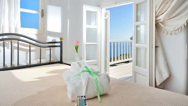 Ein Zimmer mit Bett, einem Fenster mit Meerblick und einem Balkon mit Geländer.