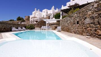 A pool area with white buildings in the background, stone walls, and lounge chairs.