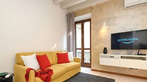 A living room with a yellow sofa, a flat-screen TV, a white cabinet, and a sliding glass door. - DesenzanoLoft Le Petit Bijou - Restyling 2025 - Downtown (Desenzano del Garda)