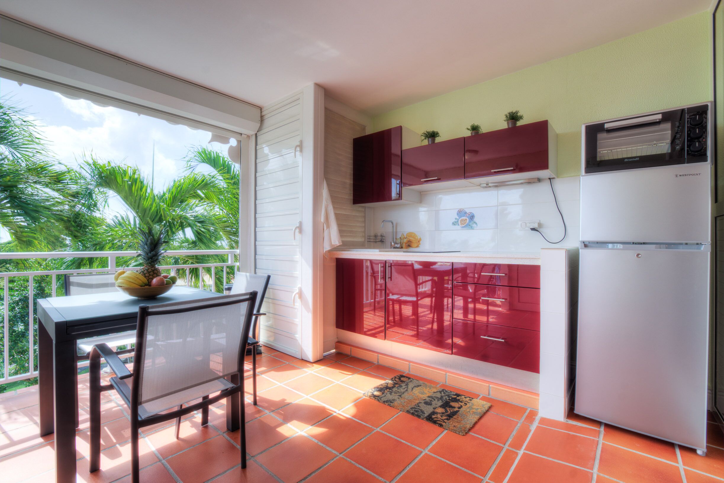A compact kitchen with a dining area, a refrigerator, and a window overlooking greenery.