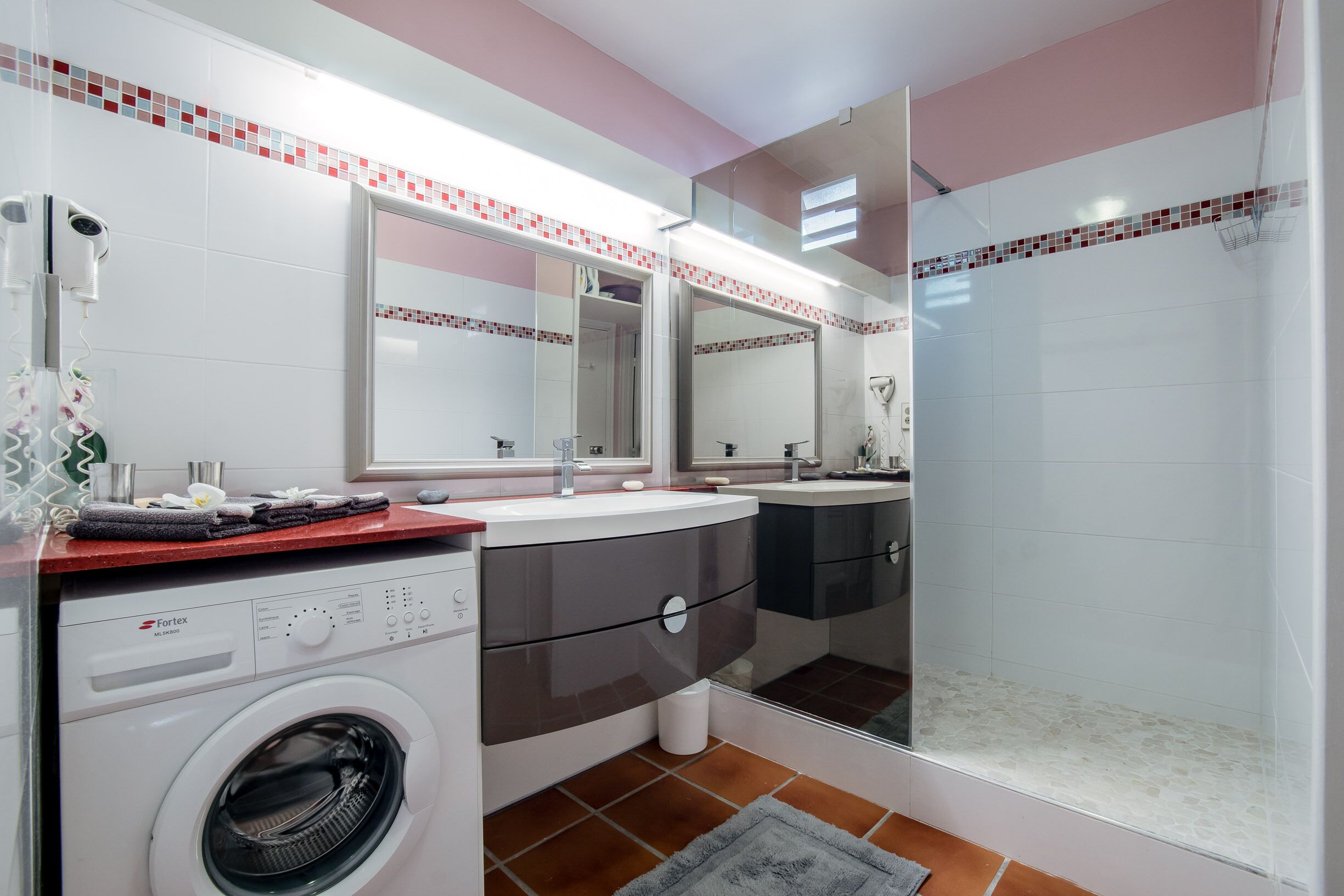 Un baño moderno con lavadora, ducha y tocador con espejo.