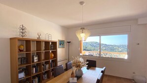 A dining area with a wooden table, chairs, a bookshelf, and a view of a hillside through a window. - Holiday rental semidetached with swimming pool in Begur, Sa Riera (Begur)