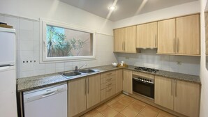 A kitchen with white cabinets, a dishwasher, a stove, and a window with a view of greenery. - Holiday rental semidetached with swimming pool in Begur, Sa Riera (Begur)