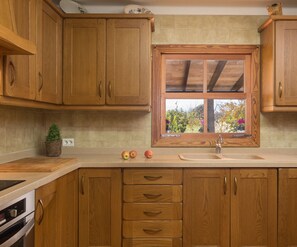 A kitchen with wooden cabinets, a window with a view of greenery, a sink, and a countertop with apples. - Casa Tonina - Beautiful villa with pool and garden in Pollença (Pollença)
