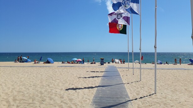 Une plage avec une promenade en bois, des drapeaux et des gens qui se détendent.
