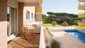 Un balcon avec une table et des chaises, une piscine et une vue sur un paysage verdoyant, avec des arbres et un bâtiment en arrière-plan.