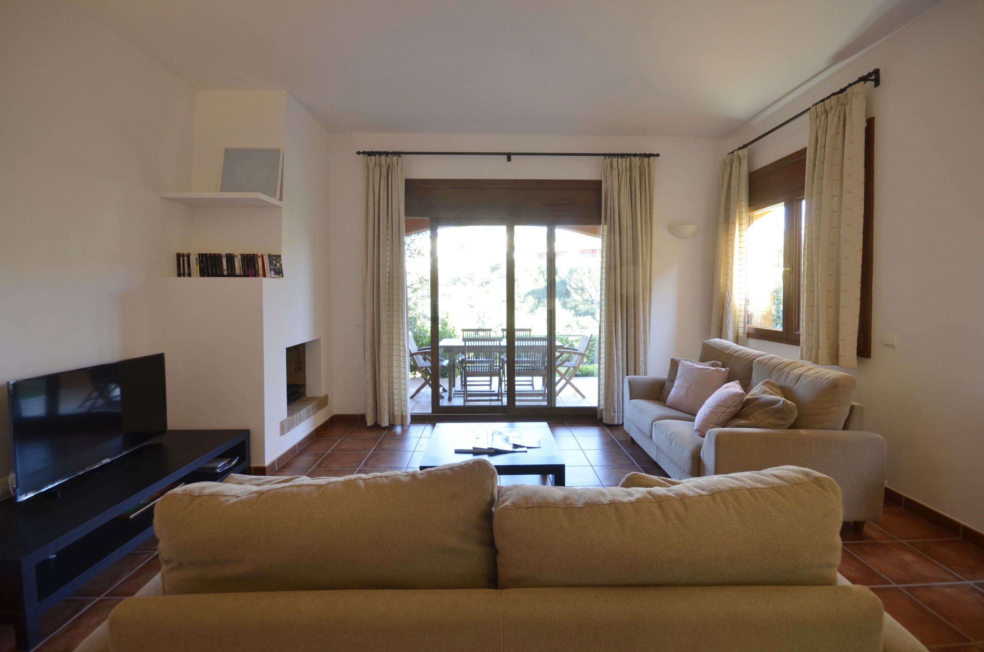A living room with a sofa, a TV, a coffee table, and a balcony with a table and chairs.