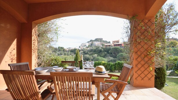 An outdoor patio with wooden furniture, a table set for dining, and a view of a hillside town. - Holiday rental semidetached with swimming pool in Begur, Centre (Begur)