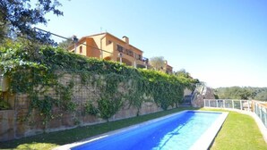 A swimming pool with a stone wall and greenery on one side, and a building with a sloped roof in the background. - Holiday rental semidetached with swimming pool in Begur, Centre (Begur)