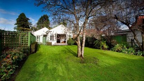 A well-maintained garden with a lawn, a wooden fence, and a house with a porch. - 200 Riccarton Holiday House (Christchurch)