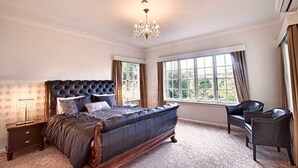 A spacious bedroom with a large bed, a chandelier, and a view of greenery through the windows. - 200 Riccarton Holiday House (Christchurch)