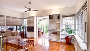 A spacious living room with a wooden floor, a sofa, a coffee table, and a bookshelf. - 200 Riccarton Holiday House (Christchurch)