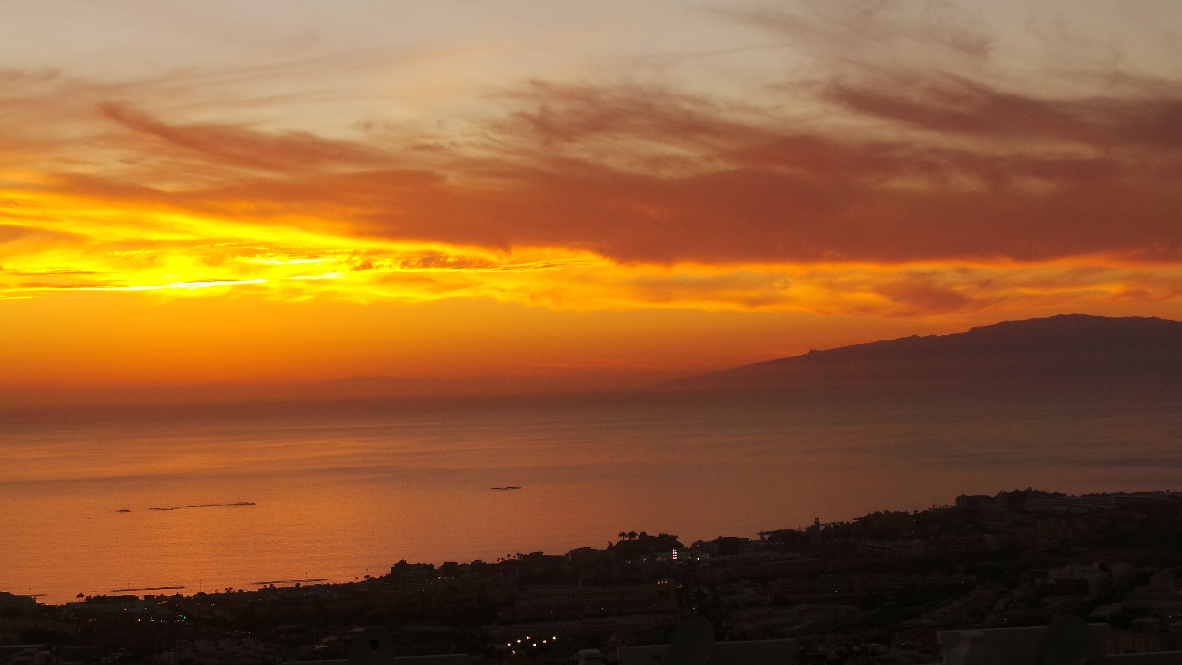 Ein Sonnenuntergang über einer Küstenstadt, im Hintergrund ein Berg.