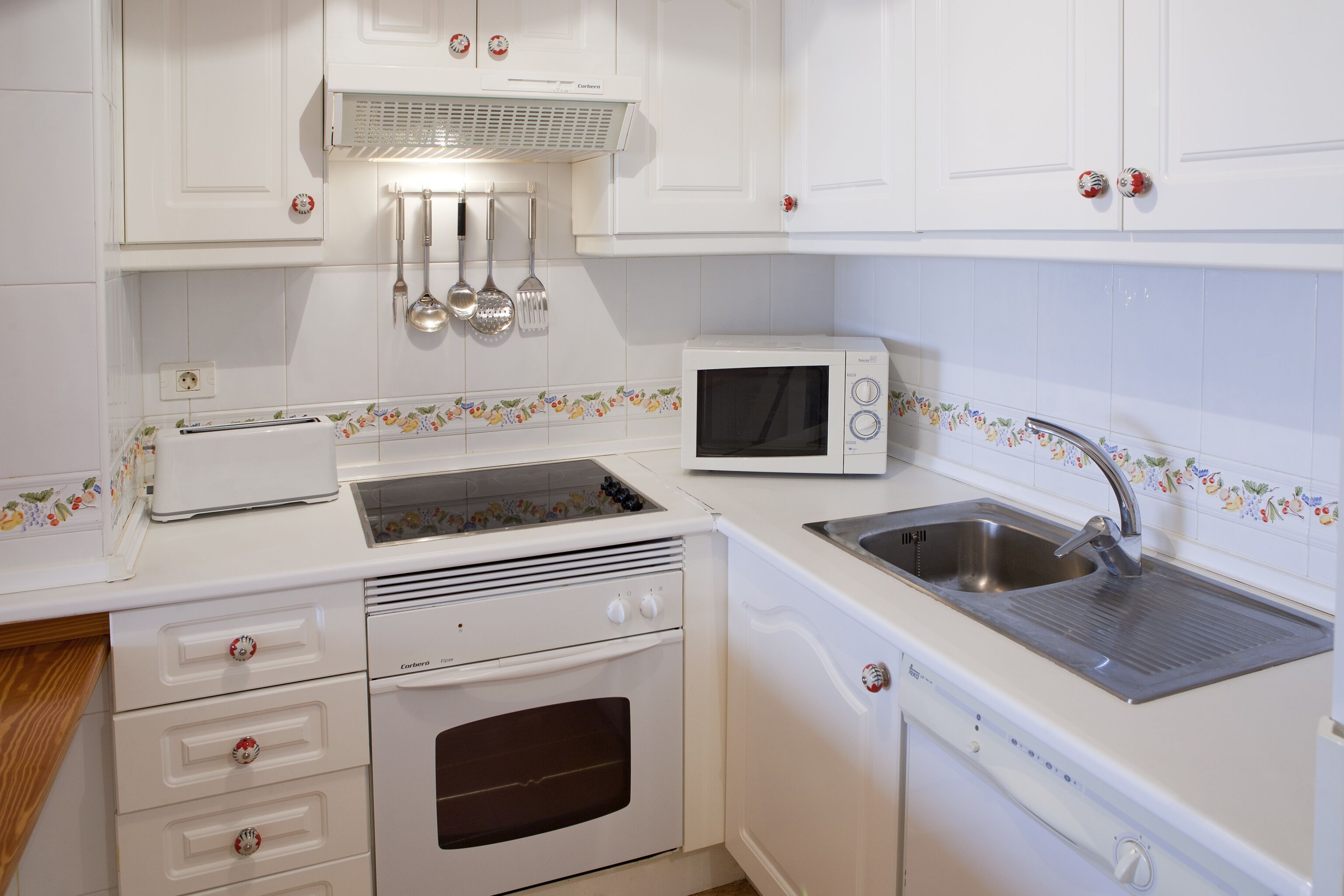 Une cuisine avec des meubles blancs, un grille-pain, un four à micro-ondes, un évier et une cuisinière.