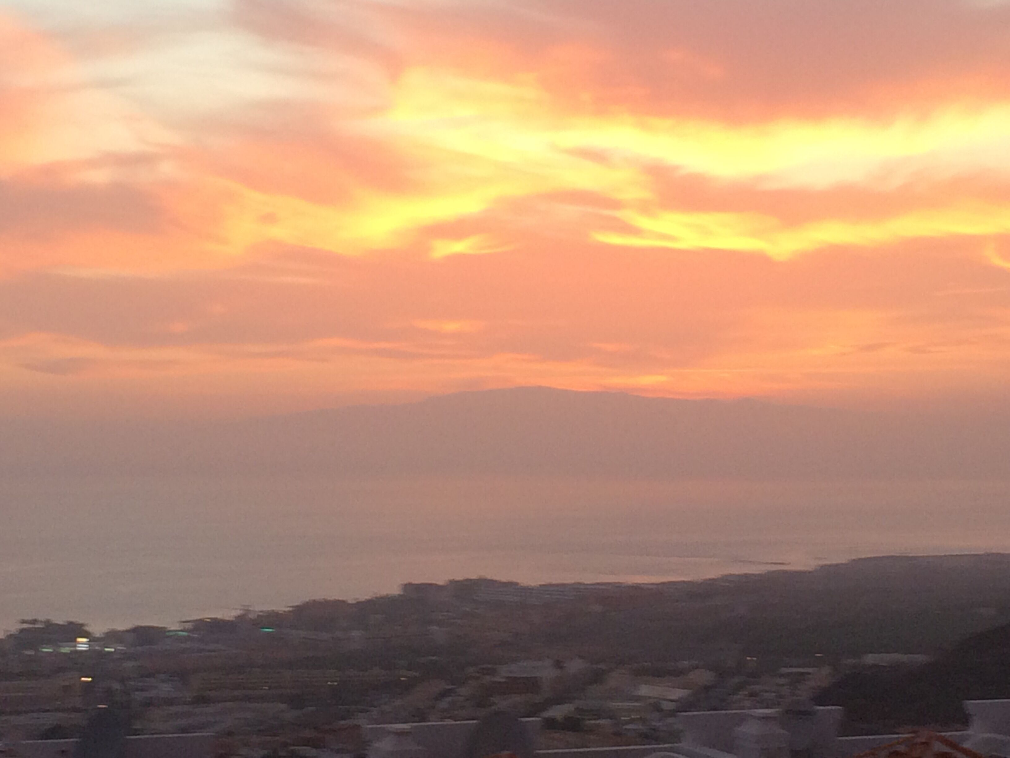 A sunset over a cityscape with buildings and a distant body of water.