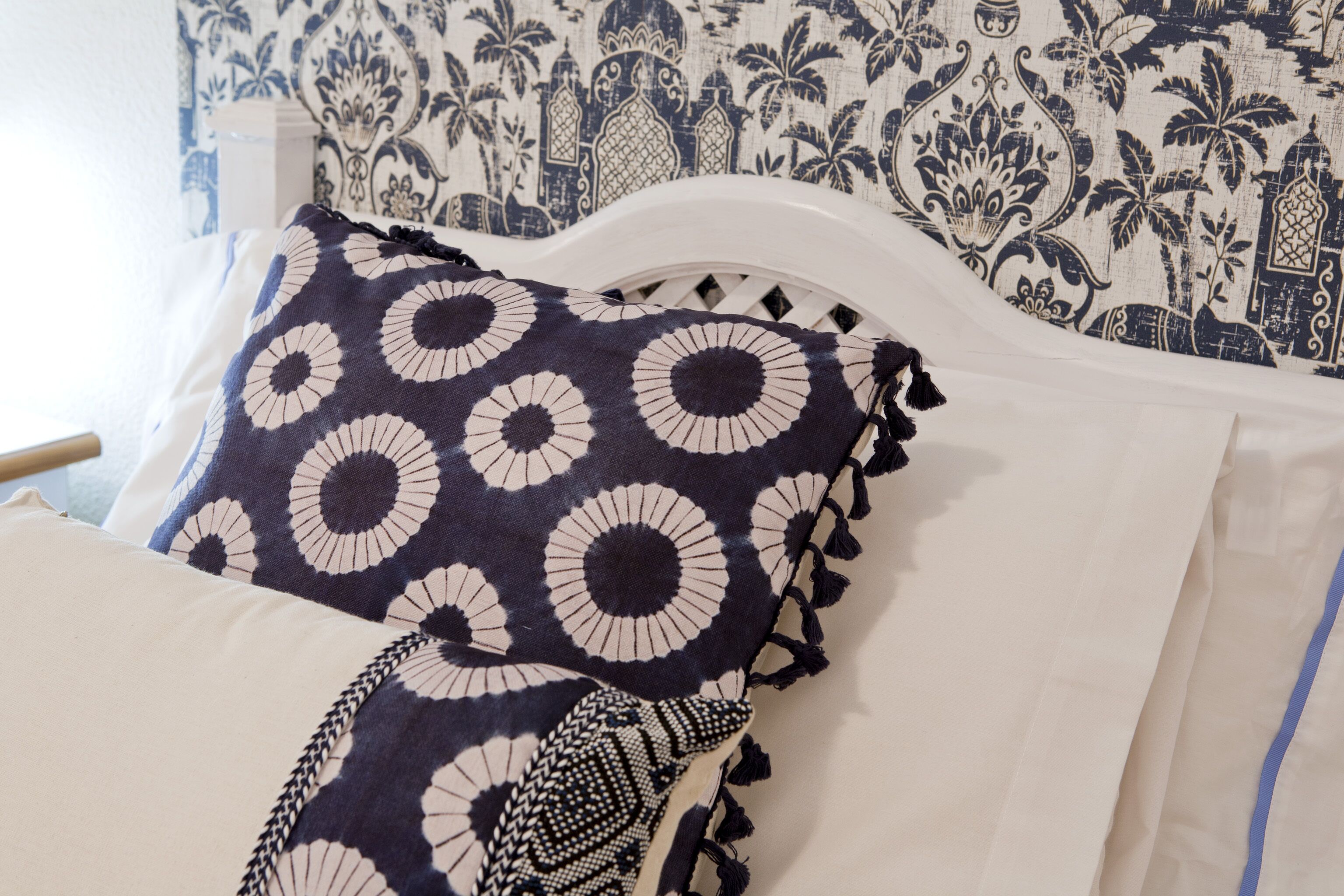 A bed with a white headboard and a patterned pillow.