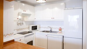 Een moderne keuken met witte kastjes, een magnetron, een spoelbak, een vaatwasser en een koelkast.