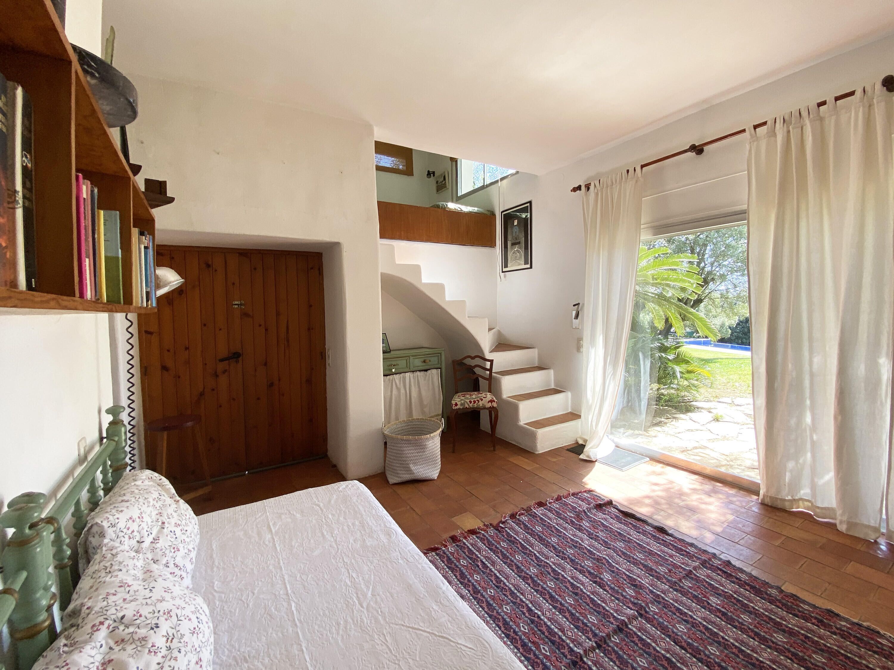 Ein Schlafzimmer mit einem Bett, einer Holztür, einer Treppe und Blick ins Freie.