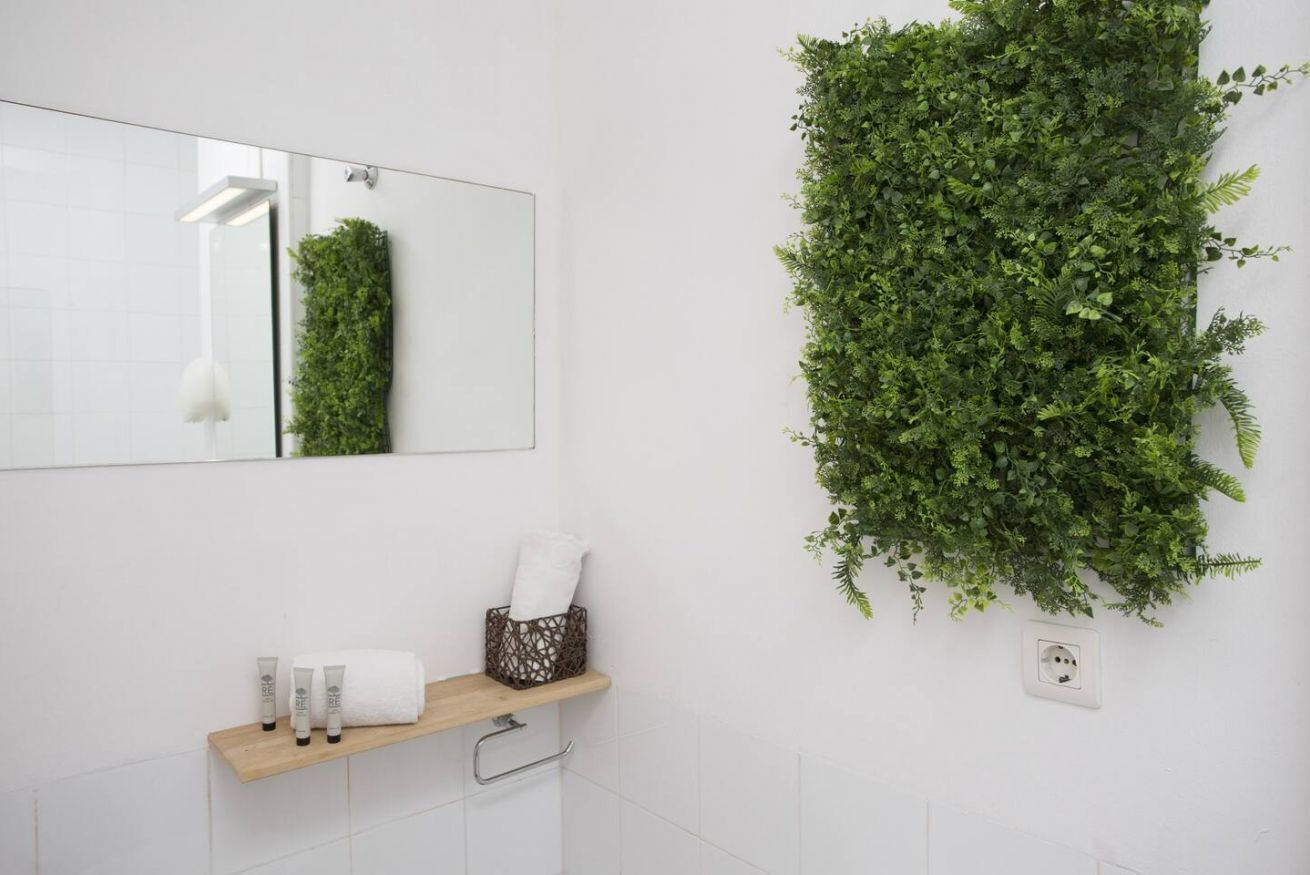 Un baño con espejo, repisas con artículos de aseo y un jardín vertical.