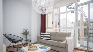 A modern living room with a white sofa, a black rocking chair, and a dining table with breakfast items. - Singular Stays Botanico 202 (València)