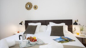 A neatly made bed with white linens, a breakfast tray with fruits and pastries, and two wall mirrors. - Singular Stays Botanico 202 (València)