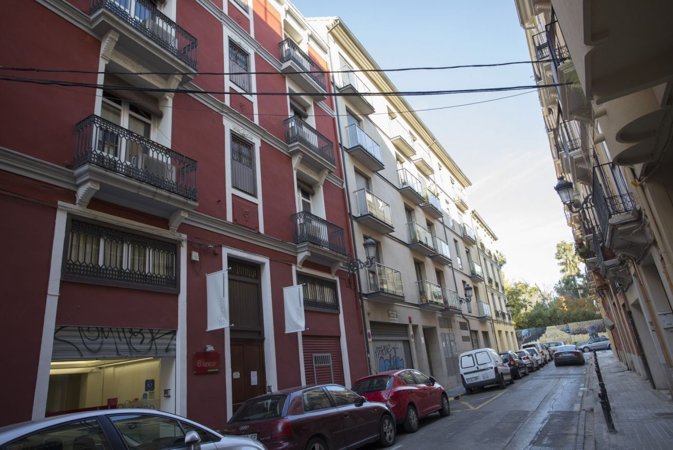 Una hilera de edificios de varios pisos con balcones, coches aparcados y un cielo despejado.