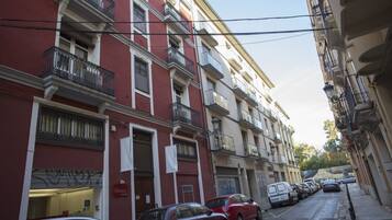 Una hilera de edificios de varios pisos con balcones, coches aparcados y un cielo despejado.