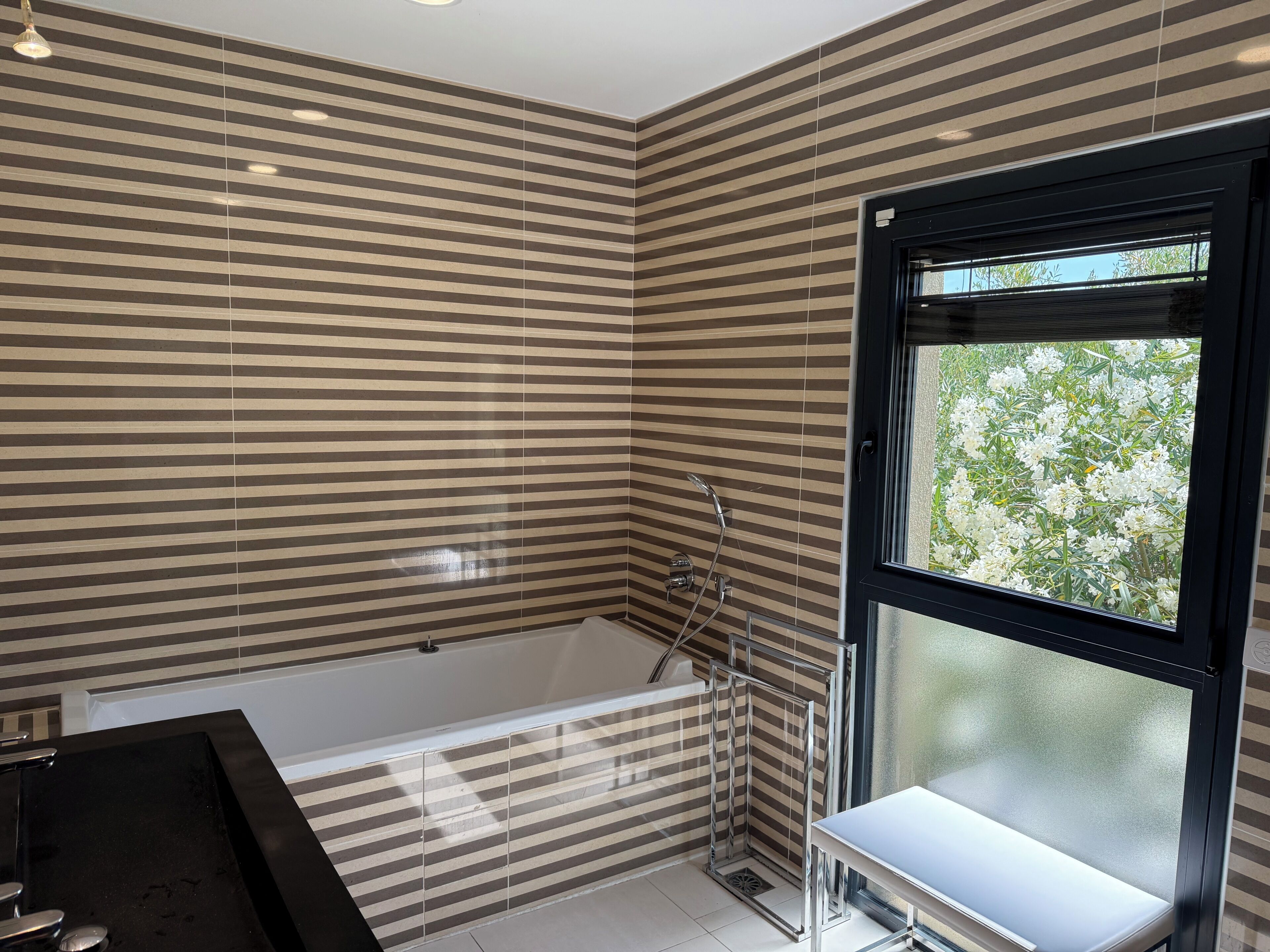 Ein modernes Badezimmer mit einer großen Badewanne, einer Duschkabine und einem Fenster mit Blick auf Grünfläche.