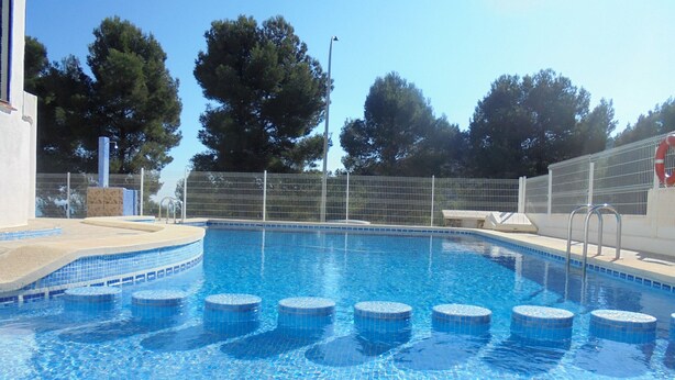 Una piscina con agua azul cristalina, rodeada por una valla y árboles.