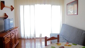 Una sala de estar con un sofá, un televisor sobre un mueble de madera y un ventanal con cortinas.