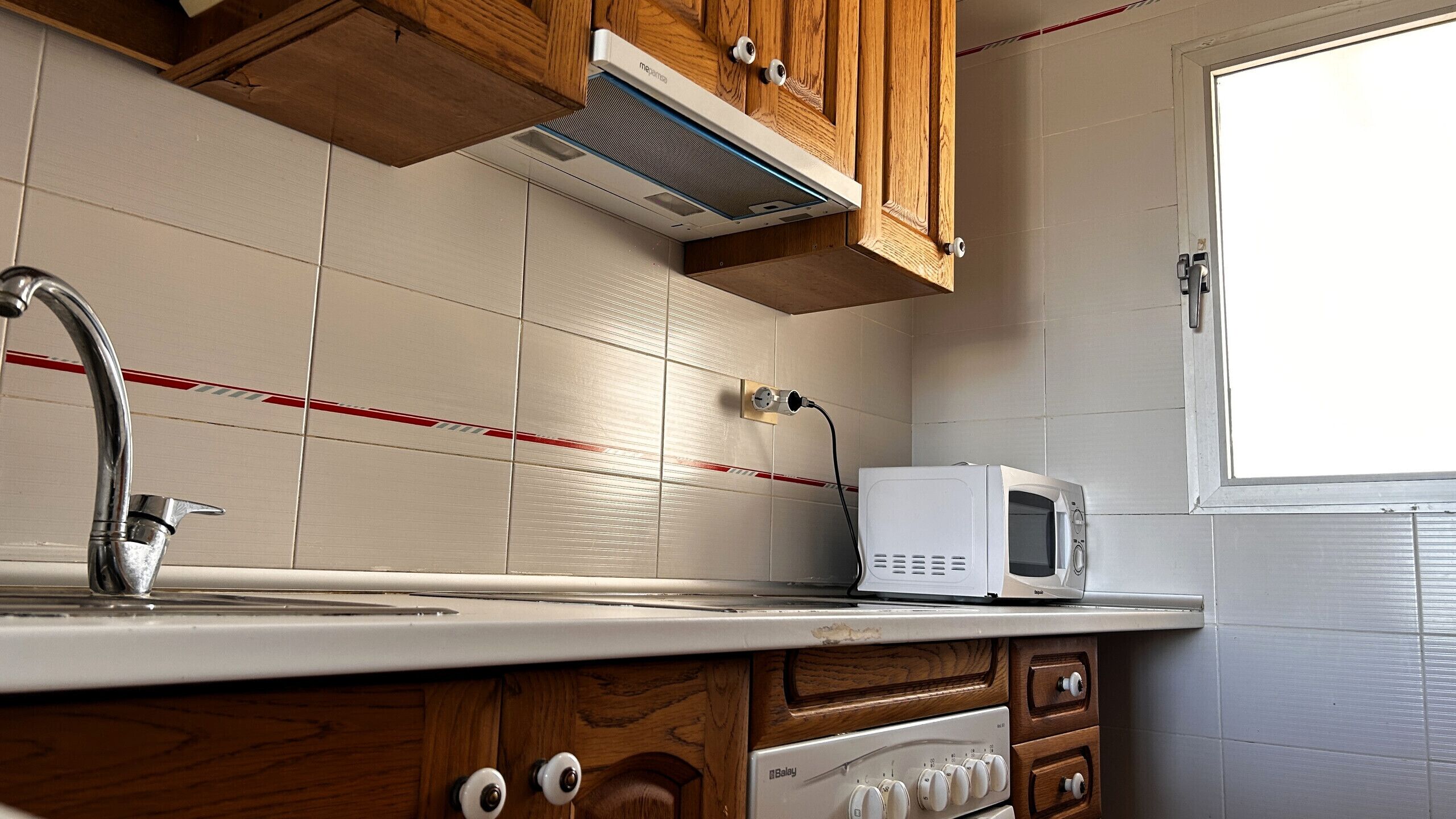 Una cocina compacta con microondas, pileta y muebles de madera.