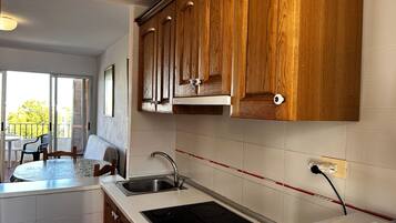 Een keuken met houten kastjes, een spoelbak en een eethoek met een tafel en stoelen.