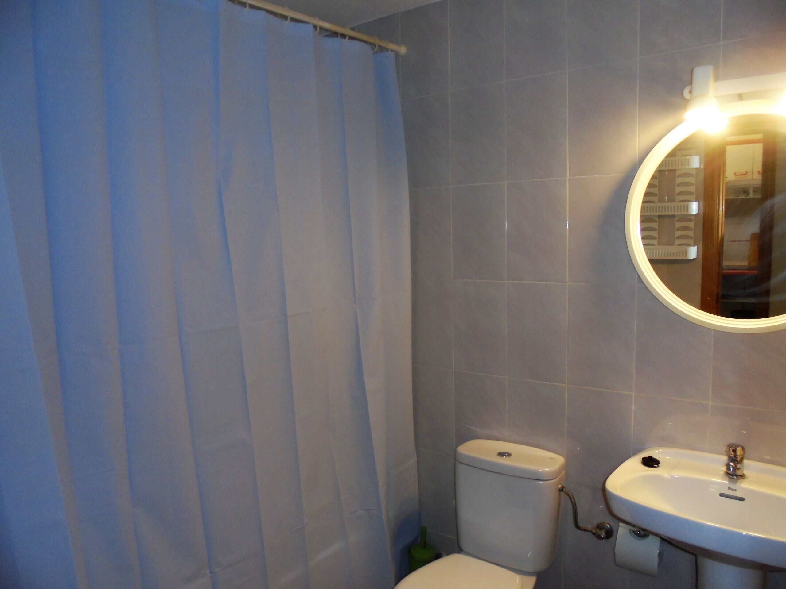 A bathroom with a toilet, sink, and a mirror with a light.